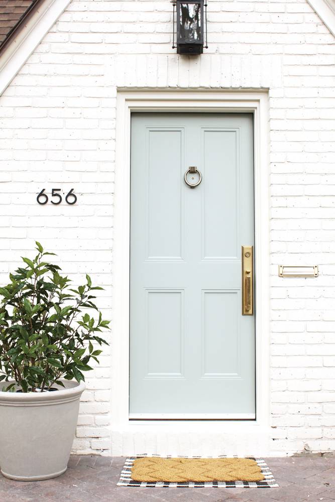 Entrada con puerta principal celeste, planta al lado y tapetes bonitos