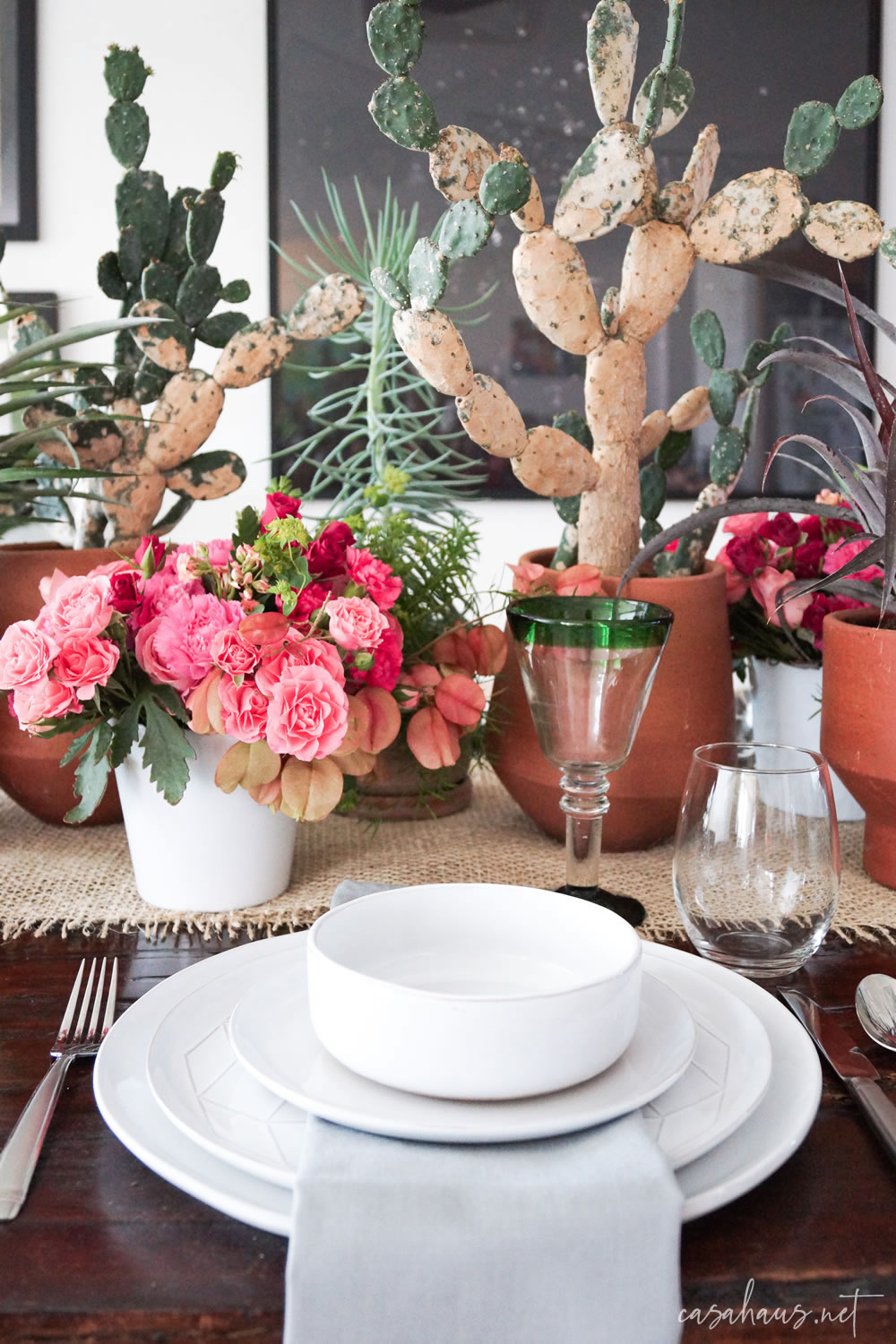Platos puestos en mesa con cactus y flores rosas